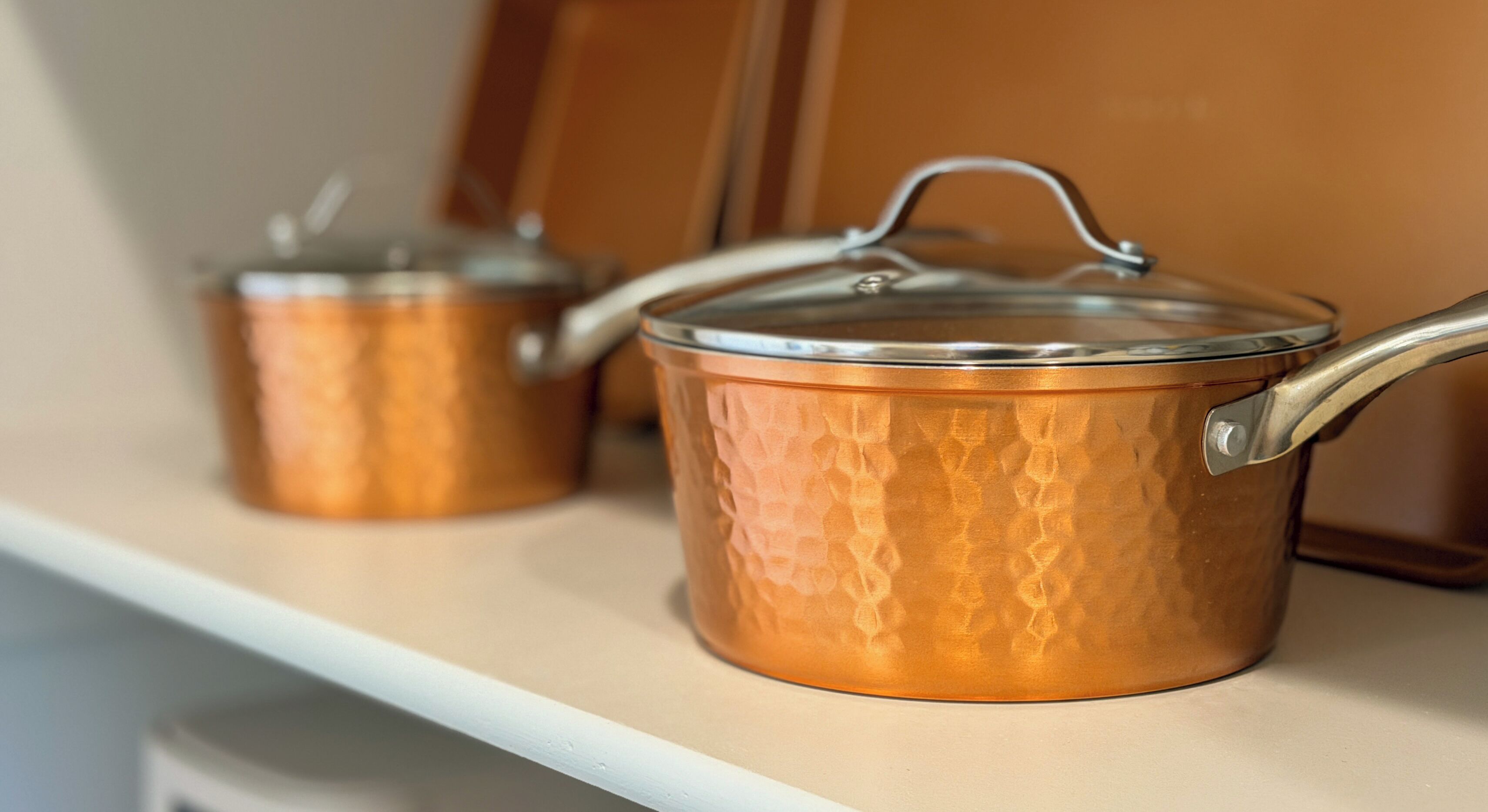 Two copper pots with lids on a shelf.