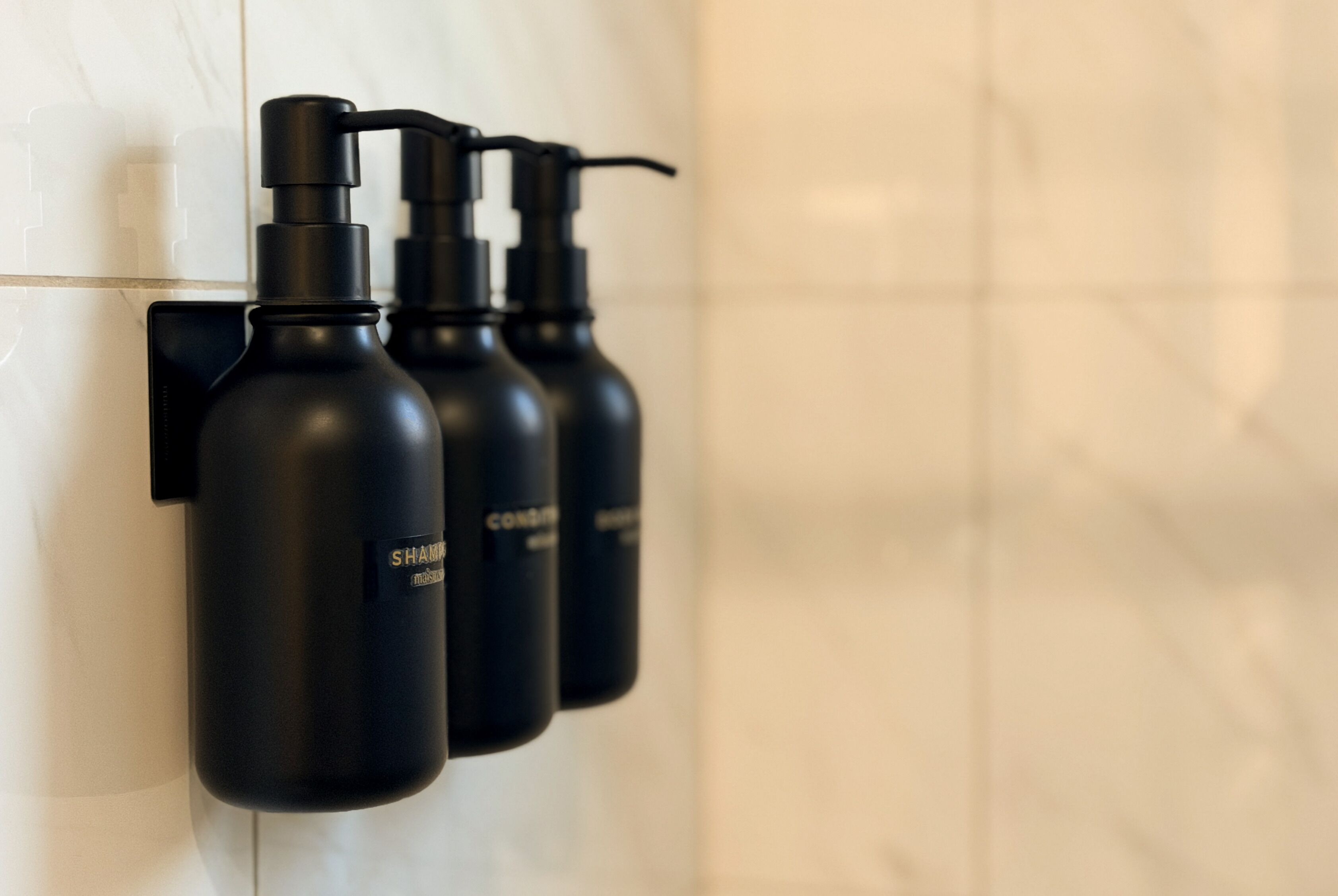 Three black bottles with pump dispensers mounted on a white tiled wall.