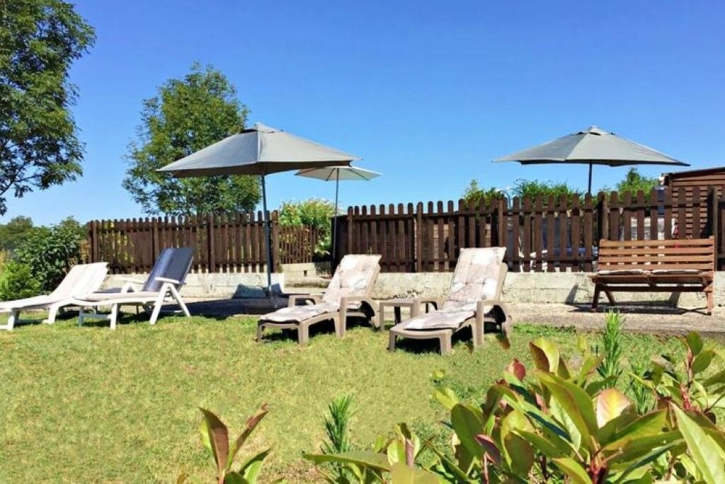 A backyard with four lounge chairs and two umbrellas, surrounded by a wooden fence and greenery.