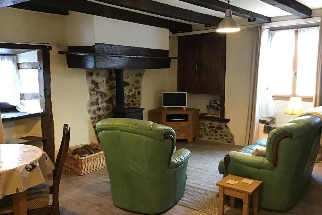 A cozy living room with a fireplace, green leather chairs, a small wooden table, and a television.