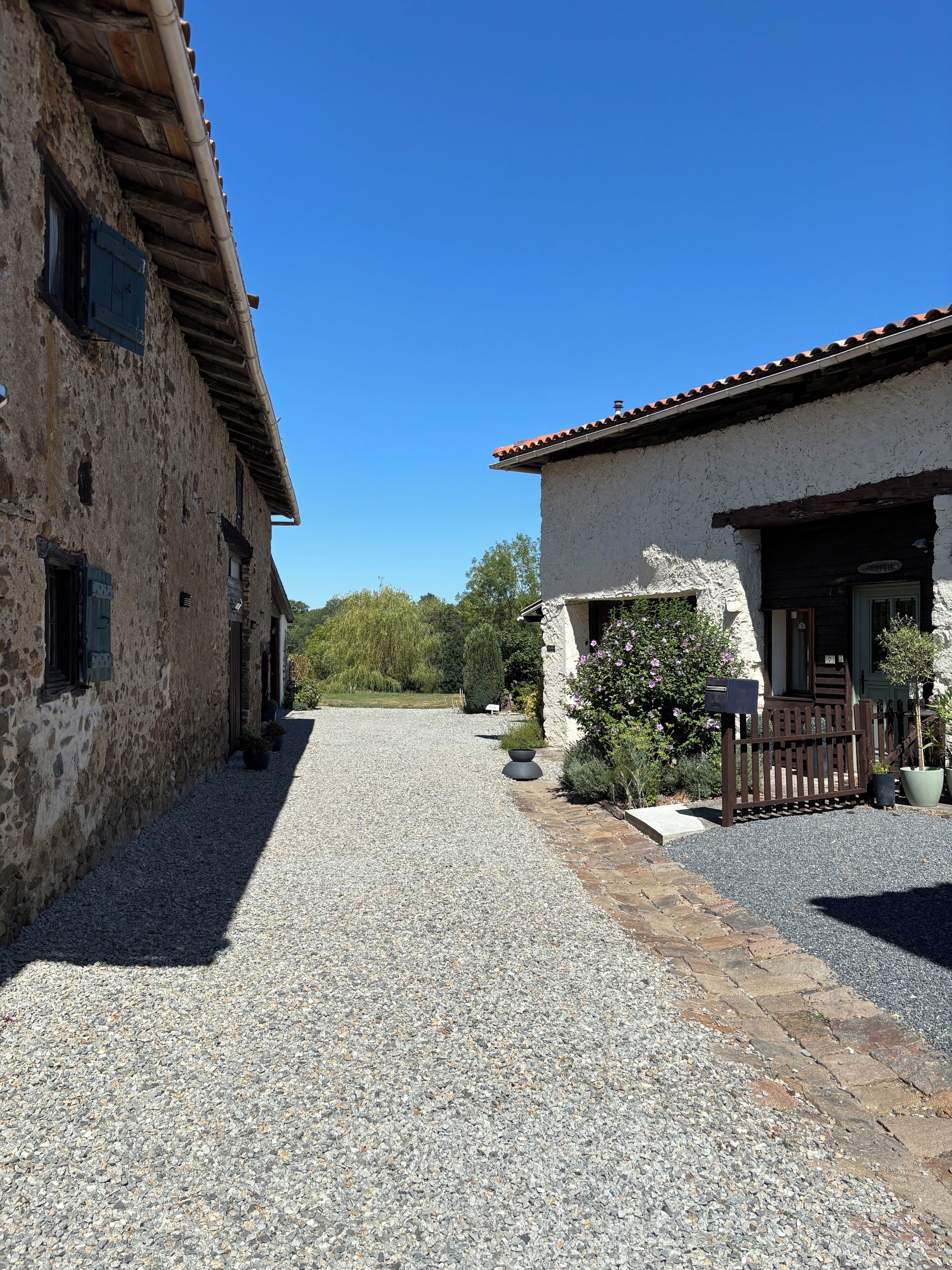 A gravel driveway leading to a building with a stone facade and a wooden fence.