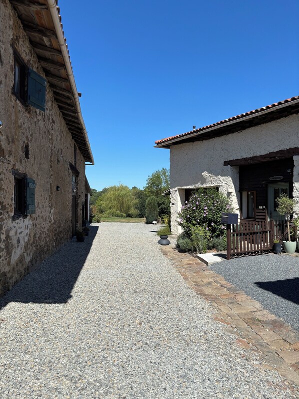 A gravel driveway leading to a building with a stone facade and a wooden fence.