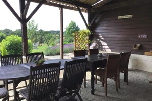 A covered patio with a wooden table and chairs, a swing set, and a sign that reads "THIS IS OUR HAPPY PLACE". - La Peruse Gite de caracterecavec piscine - 1 bedrooms - Charantaise countryside (Exideuil-sur-Vienne)