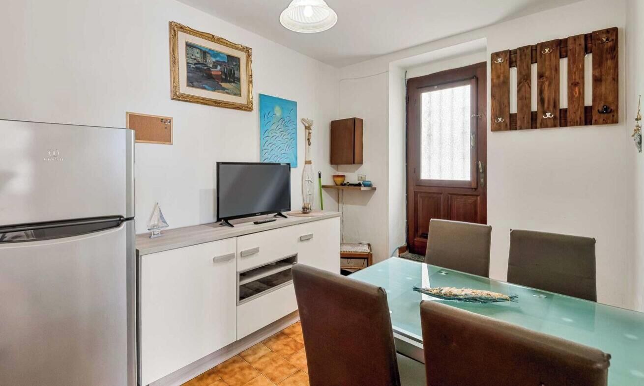 A compact kitchen with a refrigerator, a flat-screen TV, and a dining table with chairs.