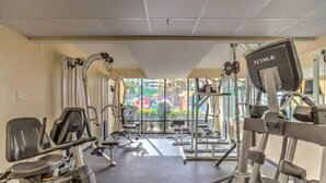 Ett gym med olika typer av träningsutrustning, inklusive löpband och styrketräningsmaskiner, och stora fönster som ger utsikt över omgivningen.