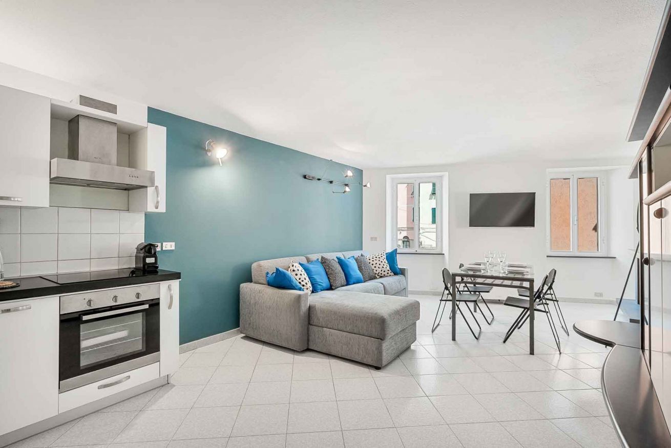 Une cuisine moderne avec un canapé gris et une table à manger, un four encastré et un mur d’accent de couleur turquoise.