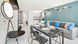 Una sala de estar moderna con una mesa de vidrio para cuatro personas, un sofá con cojines estampados y una escalera que lleva a un piso superior.