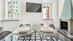 Un comedor con mesa de vidrio, sillas y televisor montado en la pared.