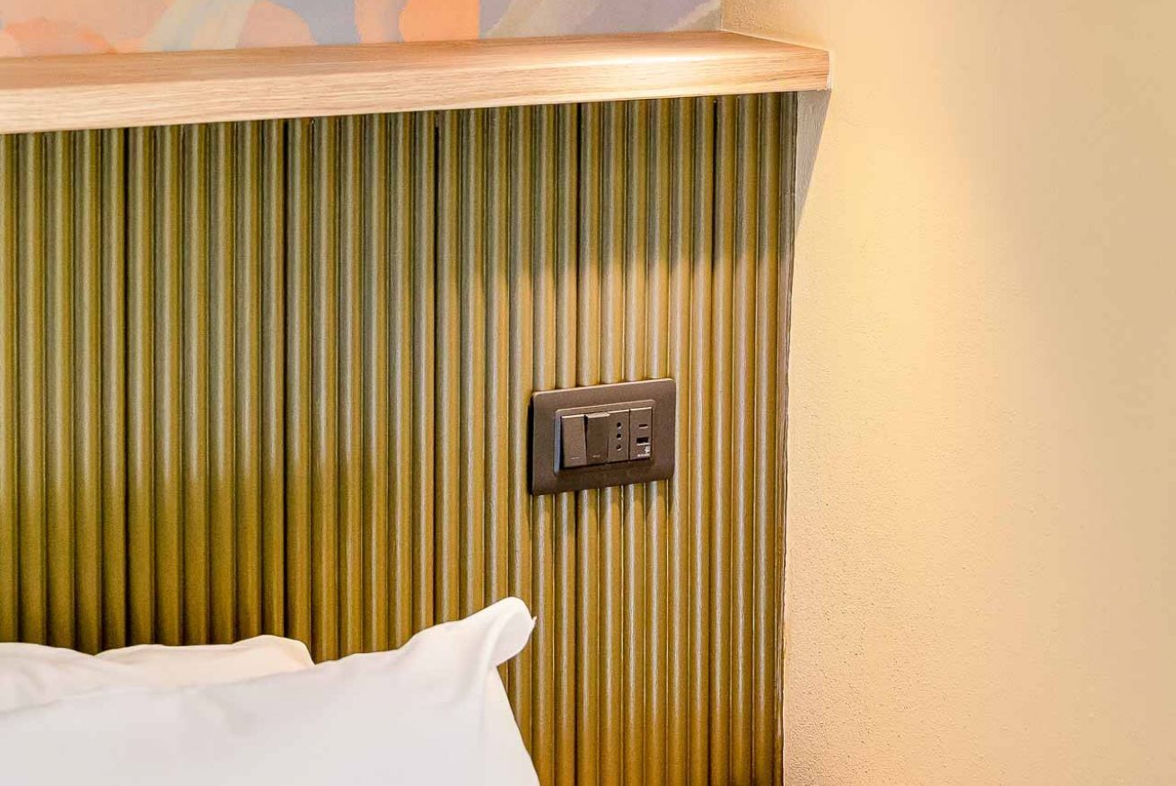 A room with a textured wall, a wooden shelf, and a power outlet.