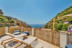 A rooftop terrace with sun loungers, a round table, and a view of the sea and hillside buildings. - Jack's Tale, Marine Lands (Manarola)