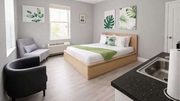 Une chambre à coucher moderne, avec un lit, une chaise, une fenêtre et des œuvres d’art accrochées aux murs.