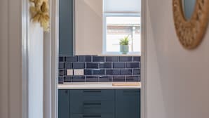 A kitchen with dark blue cabinets, a tiled backsplash, and a window with a plant on the windowsill.