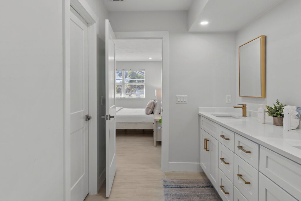 A modern bathroom with white cabinetry, a large mirror, and a view to the outside.