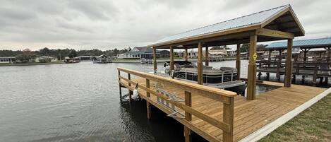 Un muelle de madera que se adentra en un lago tranquilo, con una zona de estar cubierta y un barco amarrado cerca.