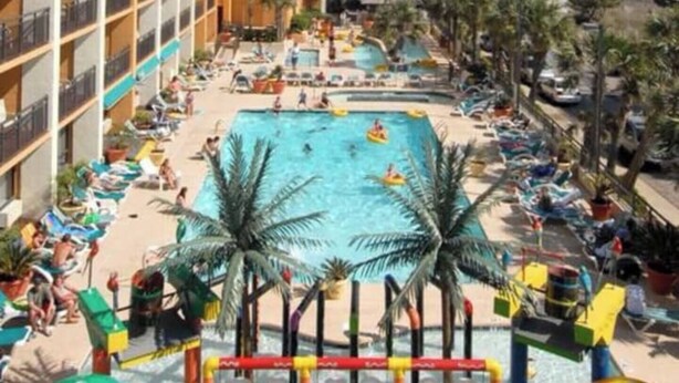 Ein Resort mit großem Pool, Palmen und Blick auf den Ozean.