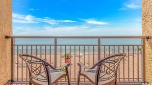 Ein Balkon mit zwei Stühlen, der auf einen Strand blickt.