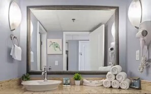Ein Badezimmer mit großem Spiegel, Waschbecken, Handtuchhalter und Fön.