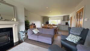 Een woonkamer met een open haard, bank, voetenbankje en een eethoek met stoelen en een tafel.
