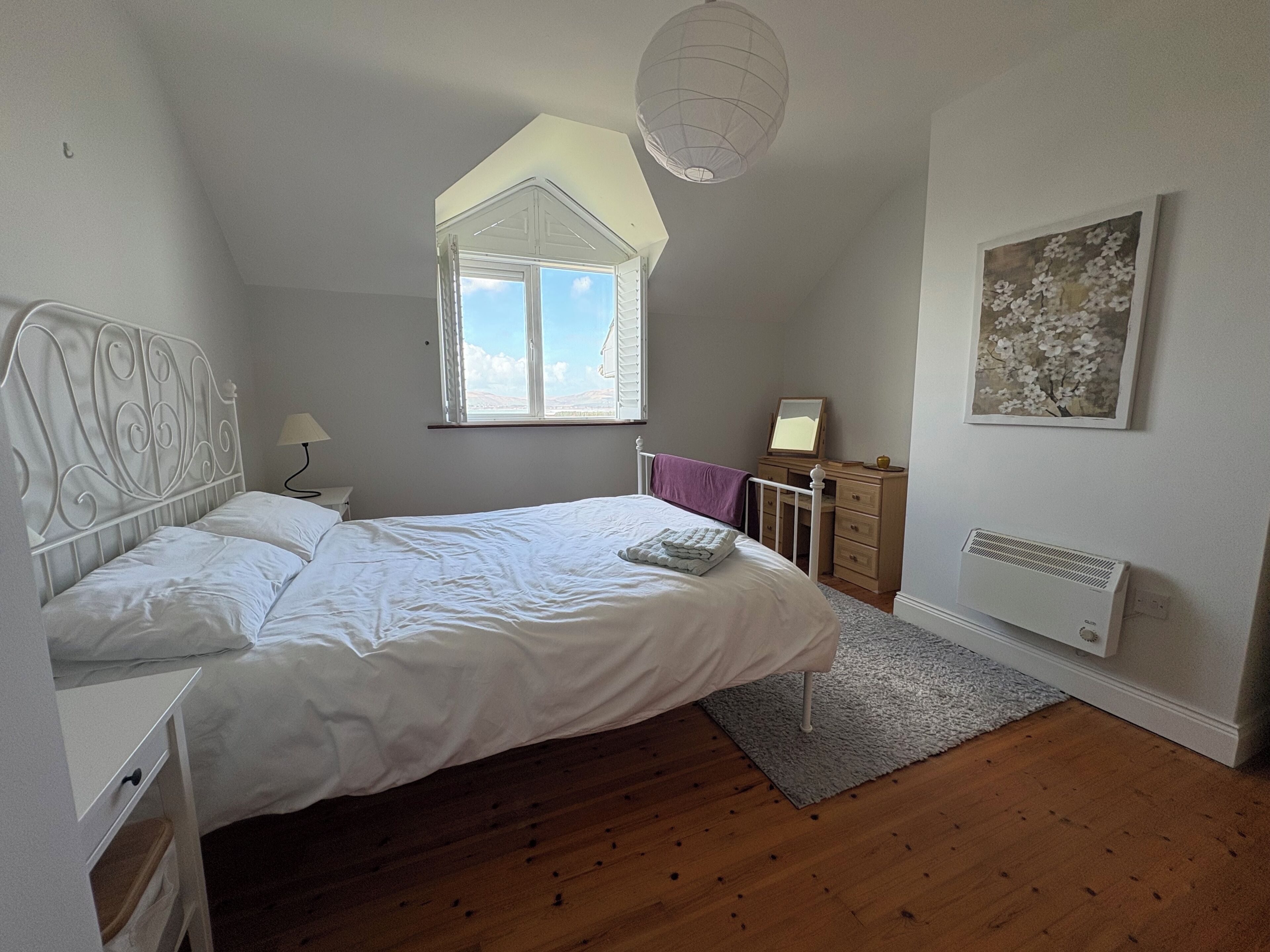 Une chambre à coucher comprenant un lit, une commode, un radiateur, une fenêtre et un luminaire fixé au plafond.