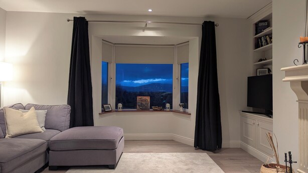 Een woonkamer met een grijze bank, een tv op een dressoir, een open haard en uitzicht op de nachthemel door een raam.