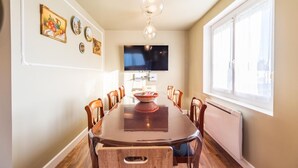 Ein Esszimmer mit einem langen Holztisch, Stühlen, einem Fernseher und Wandbildern.