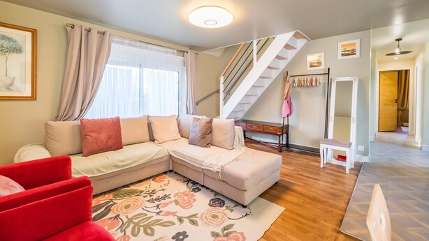 Ein modernes Wohnzimmer mit einem Ecksofa, einem roten Sessel, Holzboden, einer Treppe und einem großen Spiegel.