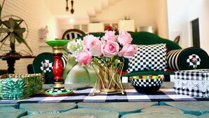 A cozy living room with a checkered tablecloth, a green sofa with patterned cushions, a vase of pink roses, and a decorative bowl. - A 3BHK Luxury Villa with Pvt Pool, Garden Near Beach (Siolim Goa)
