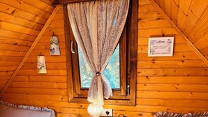 Ein gemütliches Schlafzimmer in einer Holzhütte mit zwei Betten, einem Nachttisch, einer Lampe und einem Fenster mit Vorhängen.