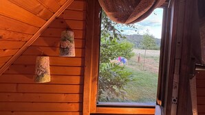 Ein gemütliches Blockhausszimmer mit Holzwänden, einem Fenster mit Blick auf Grünflächen, einer kleinen Heizung und rustikaler Einrichtung.