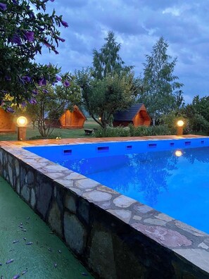 A swimming pool with stone edges, surrounded by wooden cabins and trees.