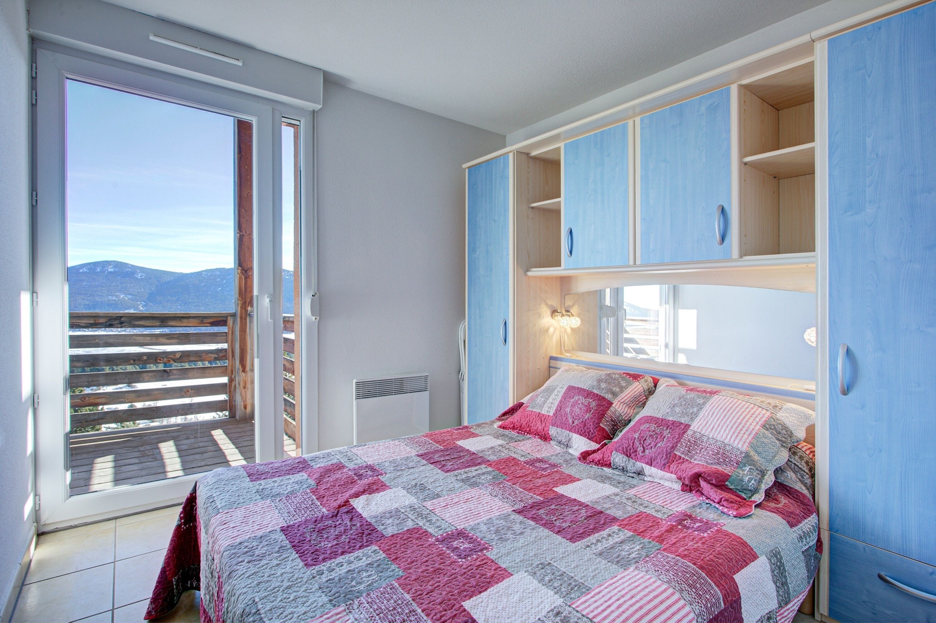 Quarto com uma cama grande, porta deslizante para uma varanda e armários embutidos de madeira.