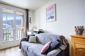 Een gezellige woonkamer met een grijze bank, een houten kast en een raam met uitzicht op een besneeerd landschap.