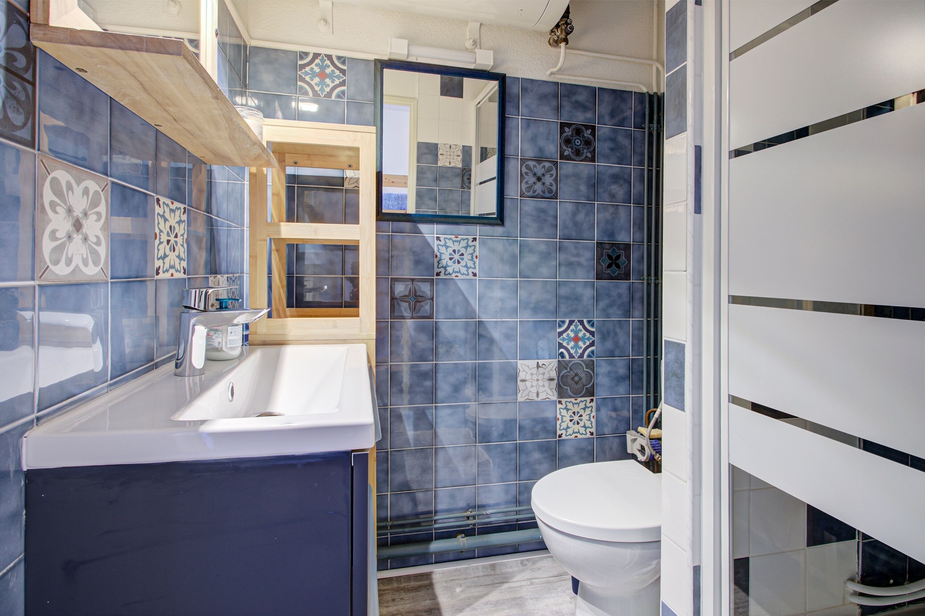 A bathroom with a blue-tiled wall, a white sink, a mirror, and a toilet.