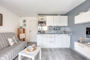 Un espacio habitable compacto con kitchenette, un sofá, una mesa de centro y una mesa de comedor.