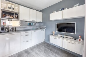 Una cocina moderna con armarios blancos, horno empotrado y microondas. Hay una cafetera y un hervidor sobre la encimera.