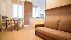 Ein Wohnzimmer mit einer Couch, einem Esstisch, Stühlen und einer Küchenzeile mit Schränken und einer Arbeitsplatte.