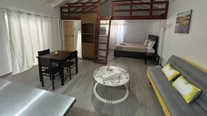 Un accogliente soggiorno con un divano, un tavolino rotondo, un tavolo da pranzo con sedie, una scala in legno e una libreria.