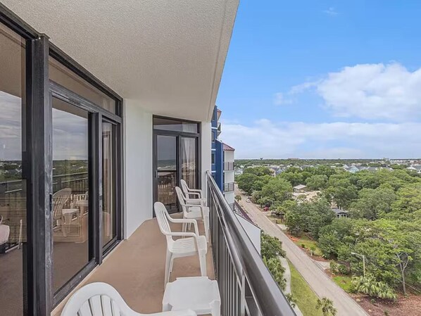 A balcony with white plastic chairs and a view of a residential area with greenery and houses. - Spacious 3-bedroom condo at Grande Shores inn serene Myrtle Beach (Myrtle Beach)