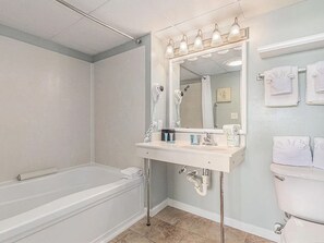 Ein Badezimmer mit Badewanne, Waschtisch mit Spiegel, Toilette und Handtüchern an der Wand.