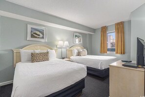 Una habitación de hotel con dos camas, un escritorio con una computadora, un televisor y dos lámparas de noche.
