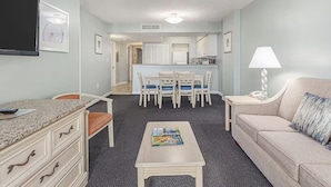A compact living space with a kitchenette, a dining area, a sofa, and a TV mounted on the wall. - Spacious 3-bedroom condo at Grande Shores inn serene Myrtle Beach (Myrtle Beach)