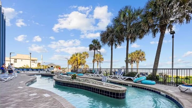 A pool area with a 3 FT depth marker, lounge chairs, and palm trees. - Spacious 3-bedroom condo at Grande Shores inn serene Myrtle Beach (Myrtle Beach)