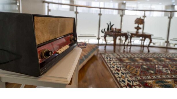 A room with a vintage radio, a patterned rug, and a wooden chair. - Elit Lara Otel (Salihli)