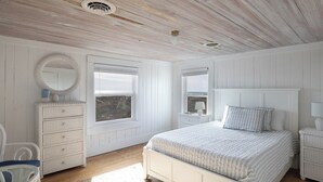 Une chambre à coucher avec un grand lit, deux fenêtres, une commode, une chaise et une table de chevet.