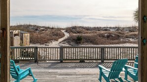 Une terrasse en bois avec des chaises, une vue sur un sentier menant à la plage et un paysage de dunes de sable.