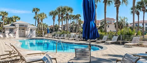A pool area with lounge chairs, umbrellas, and palm trees.
