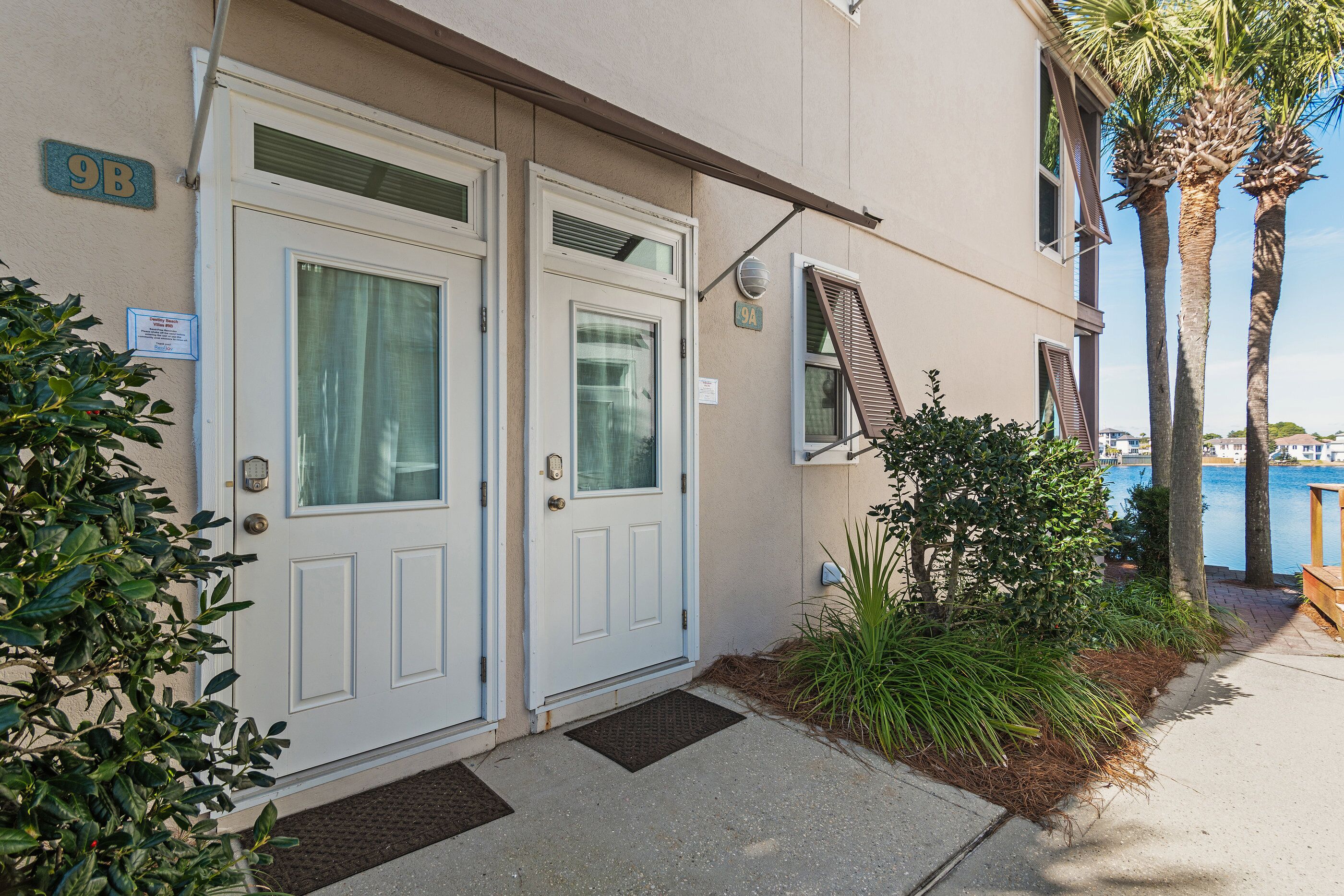 A residential building with two white doors, a small window with a shutter, and a sign indicating the address as 9B.