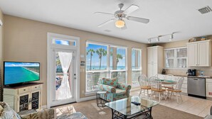 A living room with a television, a ceiling fan, and a view of the ocean through large windows. - ☀️Steps to Beach🌴Pool+Lake View | Destiny Beach Villas #9A&B☀️ (Destin)