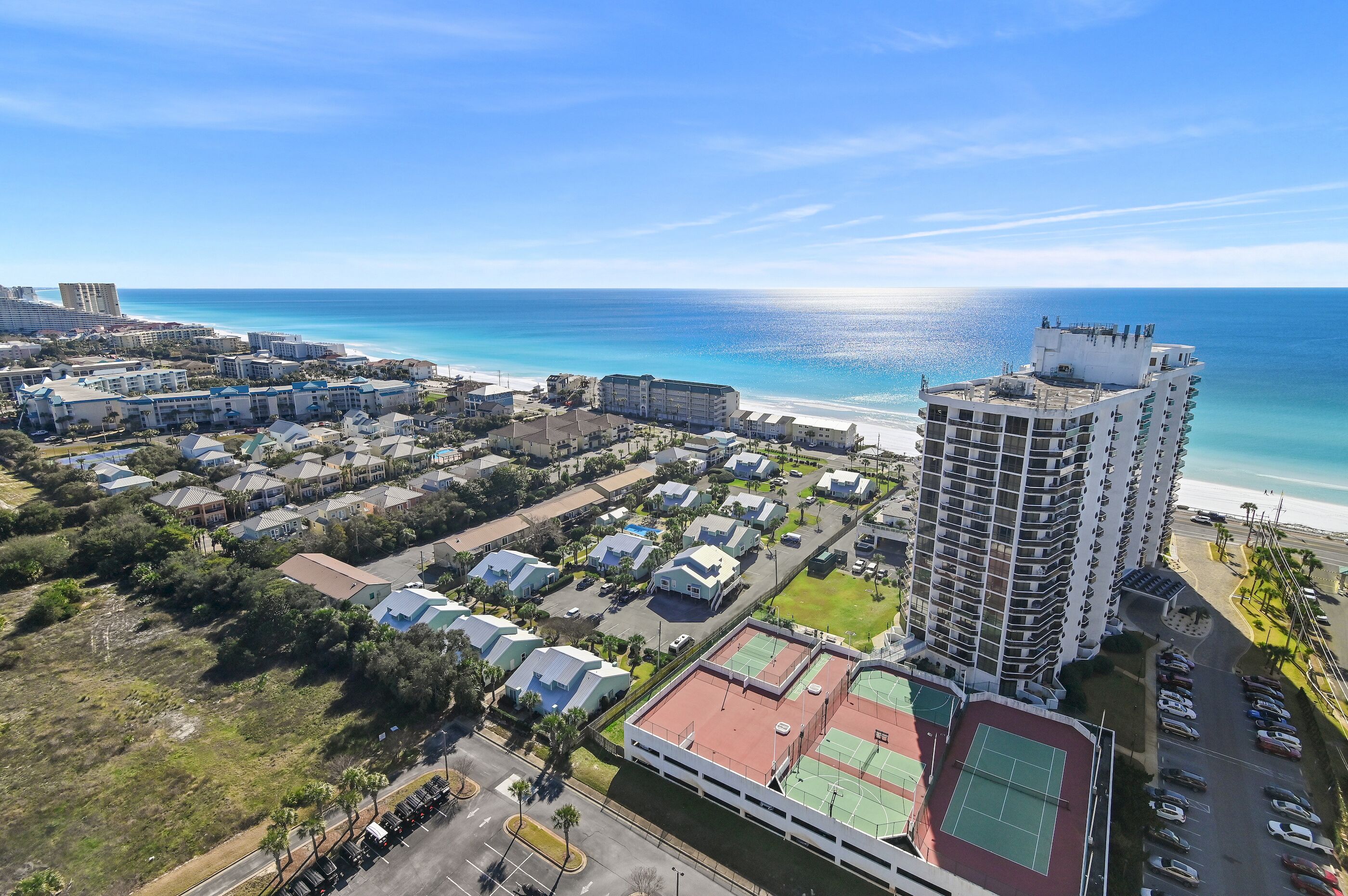 Vue aérienne d’une station balnéaire comprenant un grand hôtel, une plage et un court de tennis.