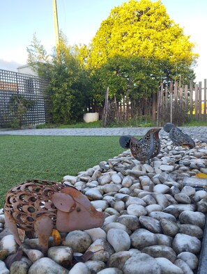 A garden area with a paved walkway, decorative metal sculptures, and a tree with yellow leaves. - Eira da Mila - 2-bedroom house with outdoor area (Coimbra)